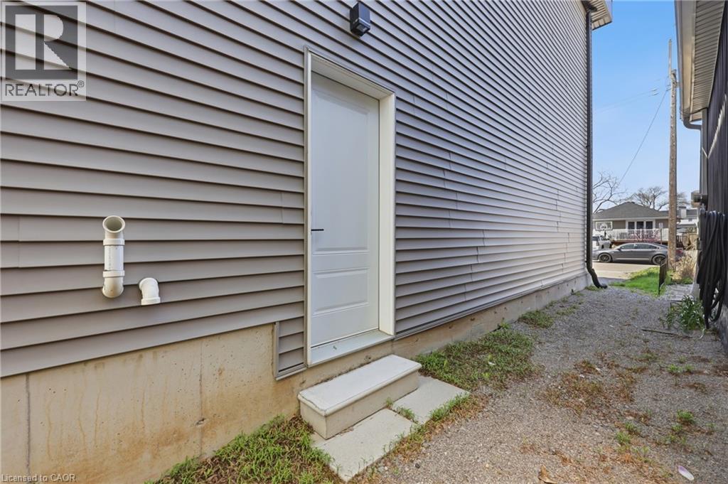 Gray horizontal siding with a white utility door, concrete foundation, and concrete steps - 37 Delena Avenue S, Hamilton, ON - Outdoor