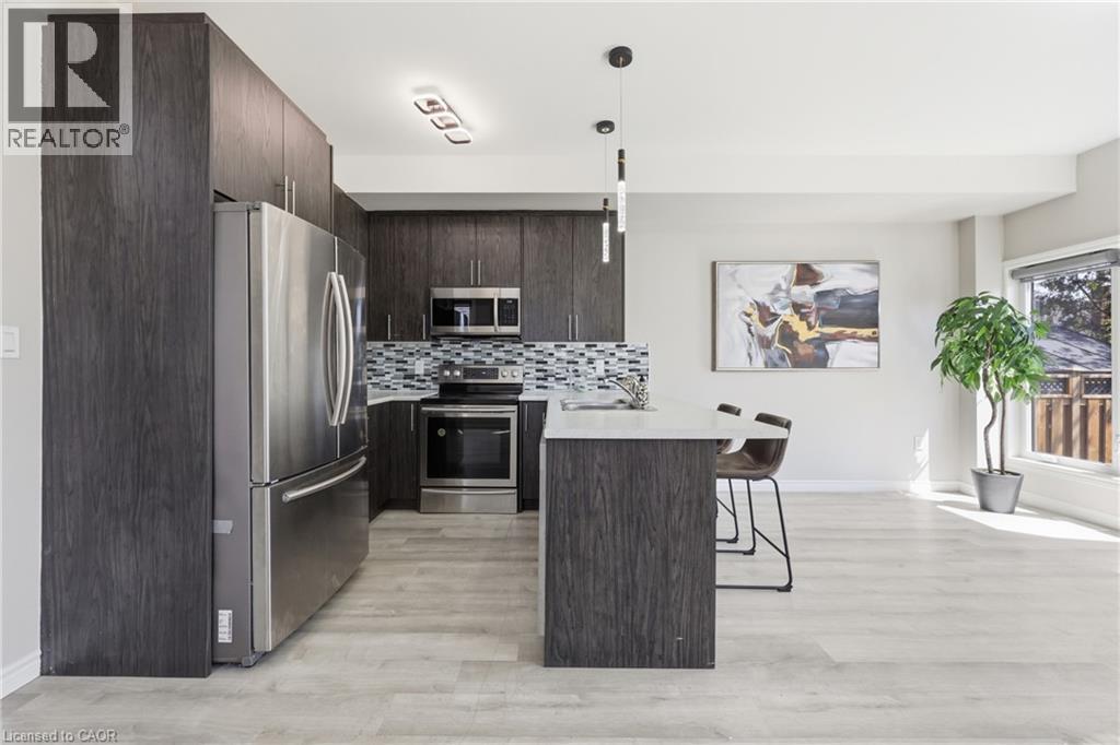 Contemporary kitchen featuring dark wood-finish cabinetry, stainless steel appliances, light-toned wood-finish flooring, a mosaic tile backsplash, and a breakfast bar with pendant lighting - 37 Delena Avenue S, Hamilton, ON - Indoor Photo Showing Kitchen With Upgraded Kitchen
