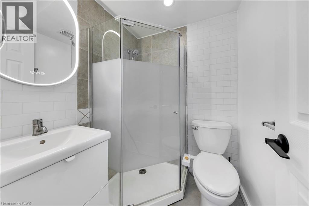 Contemporary bathroom featuring a glass-enclosed shower with frosted paneling, a white vanity with integrated sink, a backlit oval mirror, and white subway tile wainscoting - 501 Ferguson Avenue N, Hamilton, ON - Indoor Photo Showing Bathroom