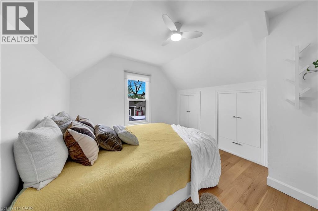 Attic bedroom featuring vaulted ceilings, wood-finish flooring, a built-in ceiling fan with integrated lighting, a window with a roller shade, and built-in storage cabinets with drawer units - 501 Ferguson Avenue N, Hamilton, ON - Indoor Photo Showing Bedroom