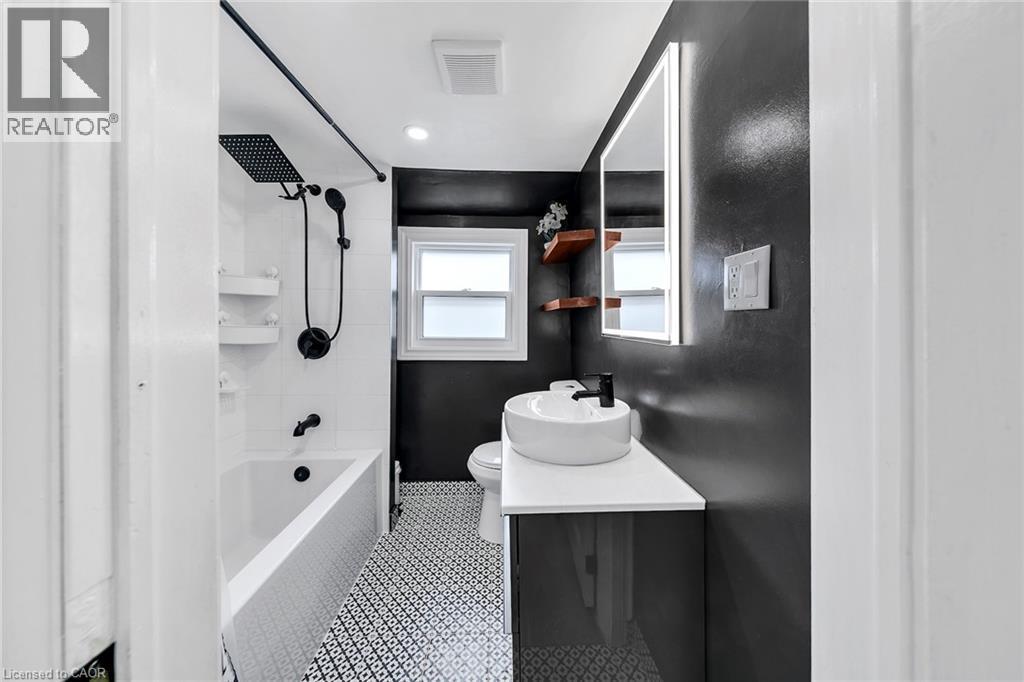Bathroom featuring a shower-over-tub combination with black fixtures, white subway tile surround, patterned floor tiles, and a floating vanity with vessel sink - 501 Ferguson Avenue N, Hamilton, ON - Indoor Photo Showing Other Room