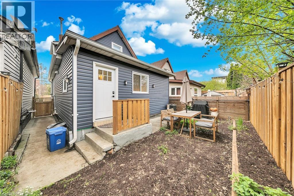 Rear exterior featuring dark gray horizontal siding, a white entry door with glass panes, and a concrete patio area with steps - 501 Ferguson Avenue N, Hamilton, ON - Outdoor