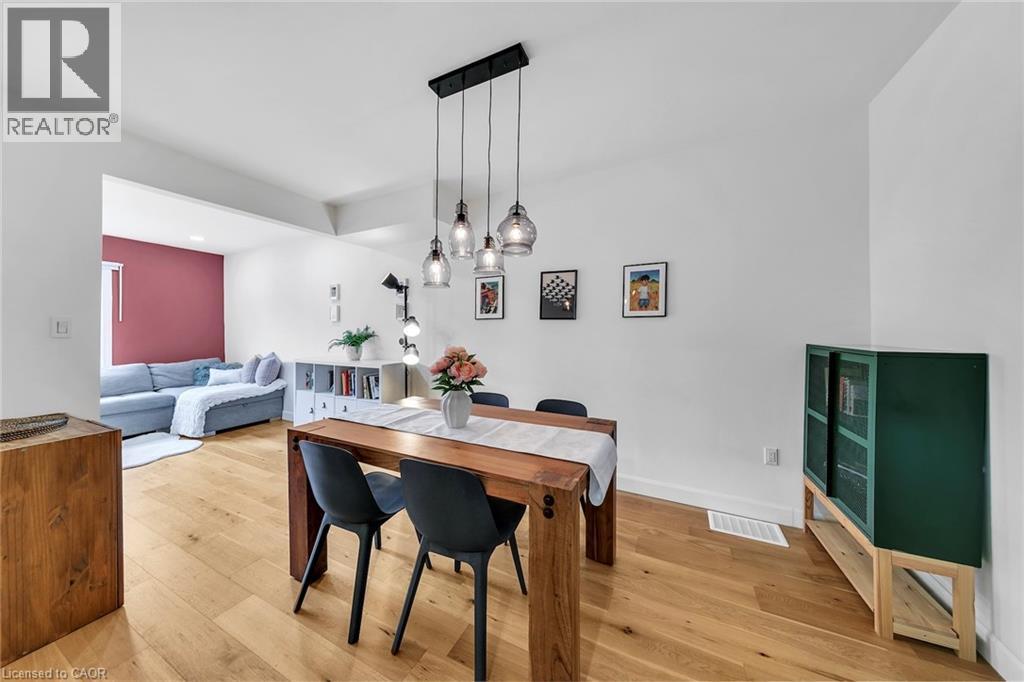 Open concept dining area featuring wood-finish flooring, a linear pendant light fixture with four glass shades, and a white painted accent wall - 501 Ferguson Avenue N, Hamilton, ON - Indoor Photo Showing Dining Room