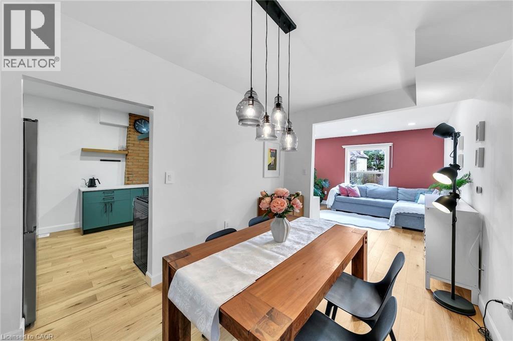 Open-concept dining area featuring wood-finish flooring, a linear pendant light fixture with clear glass shades, and a wood dining table - 501 Ferguson Avenue N, Hamilton, ON - Indoor