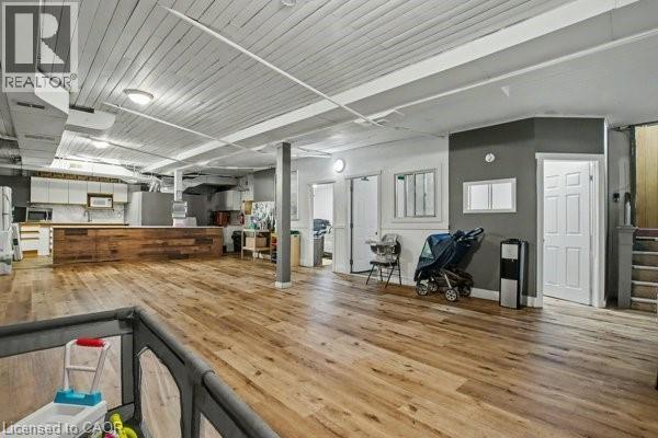 Expansive open-concept space featuring wood-finish flooring, a kitchen area with white cabinetry, a built-in wooden island, a white painted exposed beam ceiling, and recessed lighting fixtures - 37 Wellington Street, Cambridge, ON