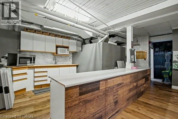 Kitchenette featuring a wood-finish bar counter, white cabinetry, a light-colored countertop, and a marbled backsplash - 37 Wellington Street, Cambridge, ON