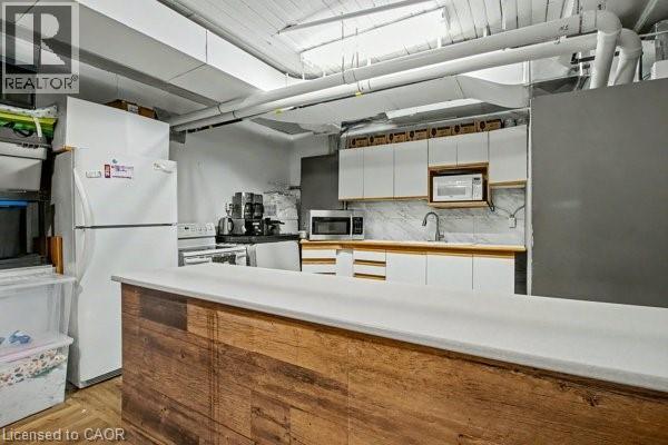 Kitchenette featuring a wood-finish bar-height counter, white cabinetry, a built-in microwave, and a stainless steel sink with a gooseneck faucet - 37 Wellington Street, Cambridge, ON