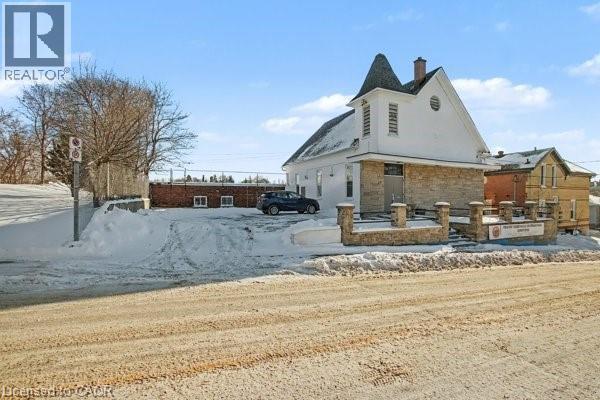Stone and white-sided building featuring a prominent steeple, gable roof, and an arched window - 37 Wellington Street, Cambridge, ON