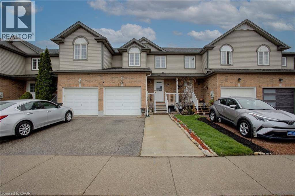 Townhome exterior featuring brick and siding facade, two white garage doors, a concrete walkway, and a covered porch with white railings - 53 Prosperity Drive, Kitchener, ON - Outdoor With Facade