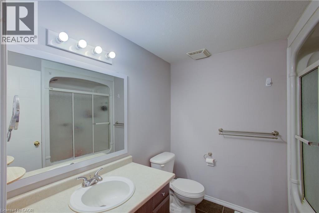 Bathroom featuring a vanity with an integrated sink, a rectangular mirror, a four-bulb vanity light fixture, and a shower with sliding glass doors - 53 Prosperity Drive, Kitchener, ON - Indoor Photo Showing Bathroom