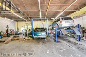 Spacious commercial garage featuring a concrete floor, high ceilings with exposed beams, and fluorescent strip lighting - 9 Meadow Lane S, Hamilton, ON
