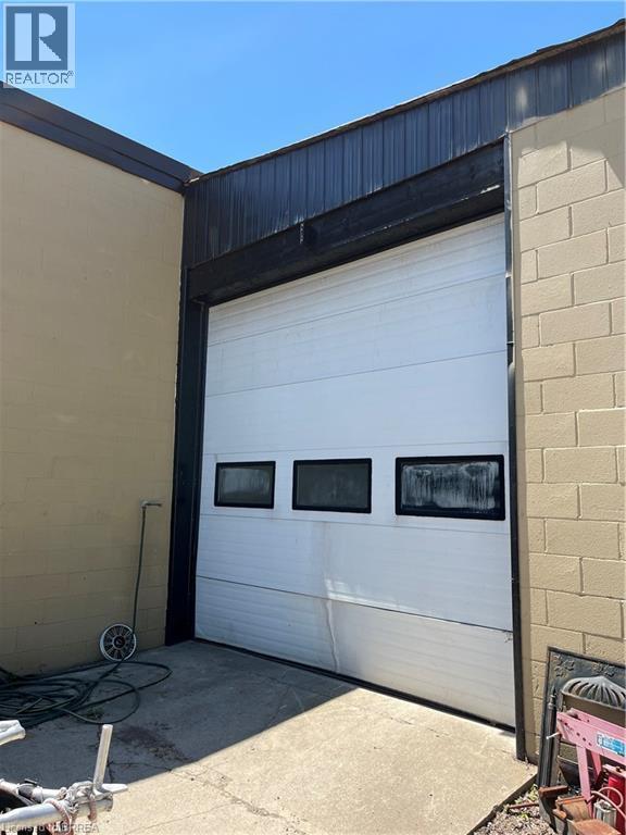 Commercial-style roll-up door with three rectangular window inserts, set into a concrete block wall exterior - 9 Meadow Lane S, Hamilton, ON