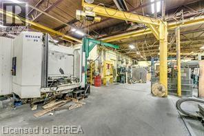 Spacious industrial interior featuring concrete flooring, exposed ceiling trusses, overhead crane systems, and substantial manufacturing equipment - 9 Meadow Lane S, Hamilton, ON