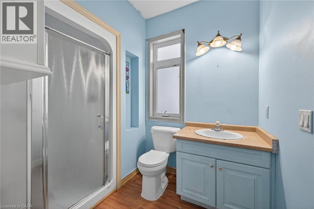 Bathroom featuring a standing shower with frosted glass enclosure, a vanity with a built-in sink and blue cabinetry, a toilet, and wood-finish flooring - 704 Stone Church Road E, Hamilton, ON - Indoor Photo Showing Bathroom