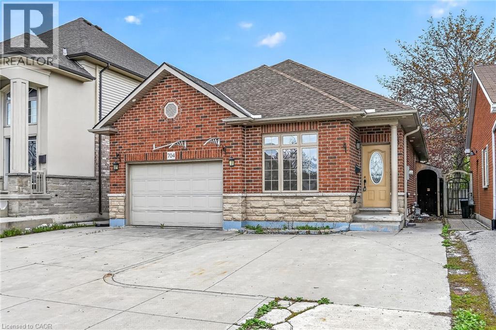 Brick and stone facade residence featuring a single-car garage with an overhead door, a concrete driveway, and a covered front entry with a decorative glass door - 704 Stone Church Road E, Hamilton, ON - Outdoor With Facade