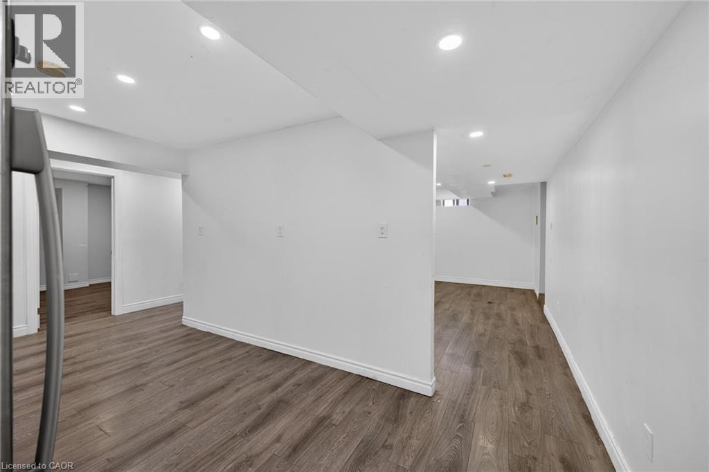 Room featuring wood-finish flooring, light grey walls, white trim, and a white paneled door - 704 Stone Church Road E, Hamilton, ON - Indoor Photo Showing Other Room