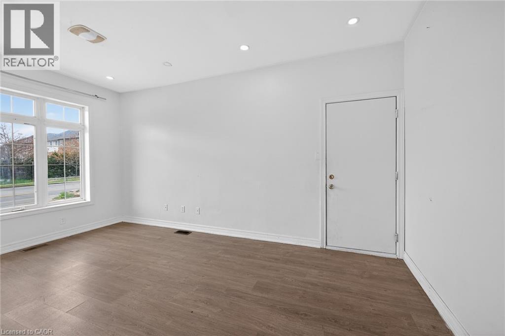Spacious room featuring wood-finish flooring, recessed ceiling lighting, a large multi-pane window, and white trim - 704 Stone Church Road E, Hamilton, ON - Indoor Photo Showing Other Room