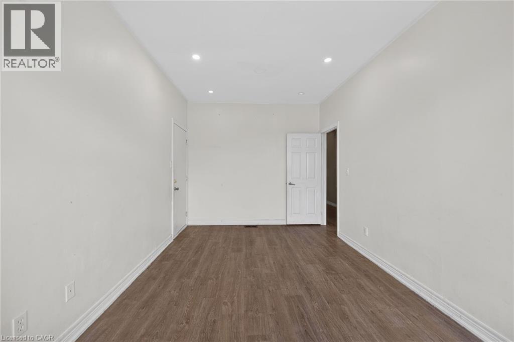 Spacious interior room featuring wood-finish flooring, recessed lighting, neutral wall tones, white trim, and a paneled door - 704 Stone Church Road E, Hamilton, ON - Indoor Photo Showing Other Room