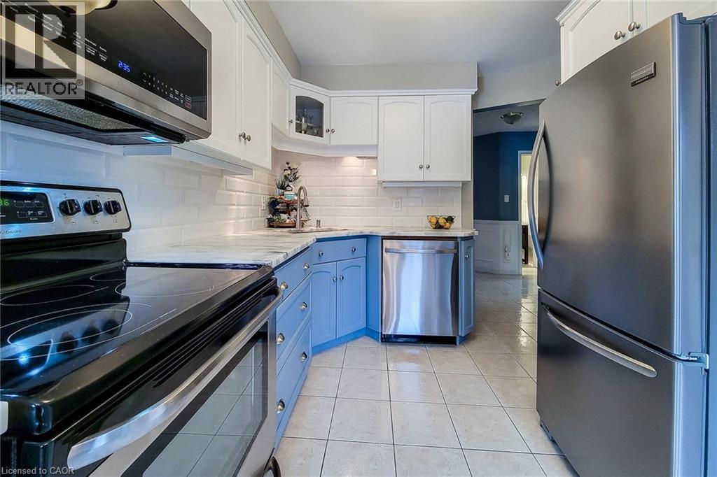 Kitchen featuring stainless steel appliances, white subway tile backsplash, light-toned countertops, two-tone cabinetry, and square tile flooring - 146 Locheed Drive, Hamilton, ON - Indoor Photo Showing Kitchen With Stainless Steel Kitchen