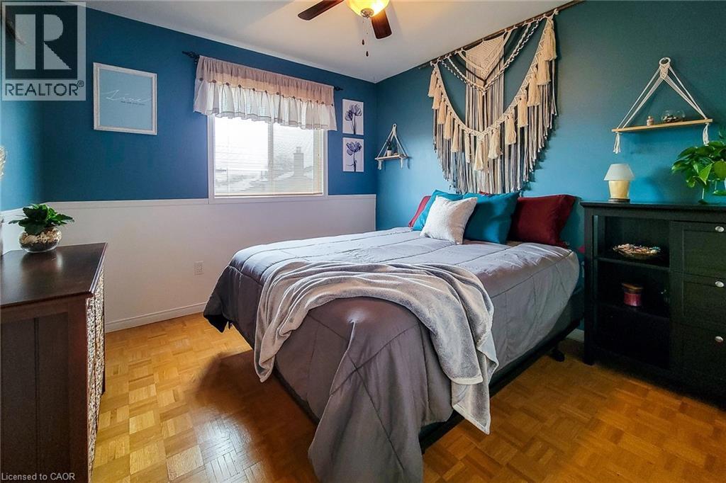 Room featuring wood-finish parquet flooring, a white-trimmed window, a ceiling fan with integrated lighting, and a two-tone wall finish with a white lower panel and blue upper section - 146 Locheed Drive, Hamilton, ON - Indoor Photo Showing Bedroom