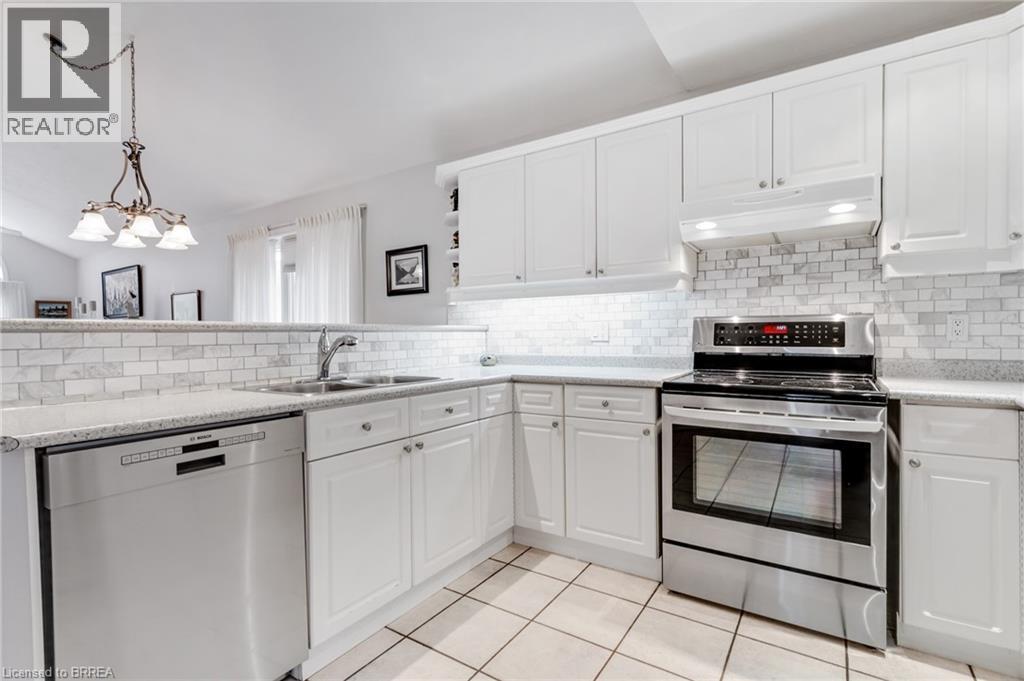 Modern kitchen featuring white cabinetry, subway tile backsplash, stainless steel appliances, a double basin sink, and tile flooring - 422 Powerline Road Unit# 10, Brantford, ON - Indoor Photo Showing Kitchen