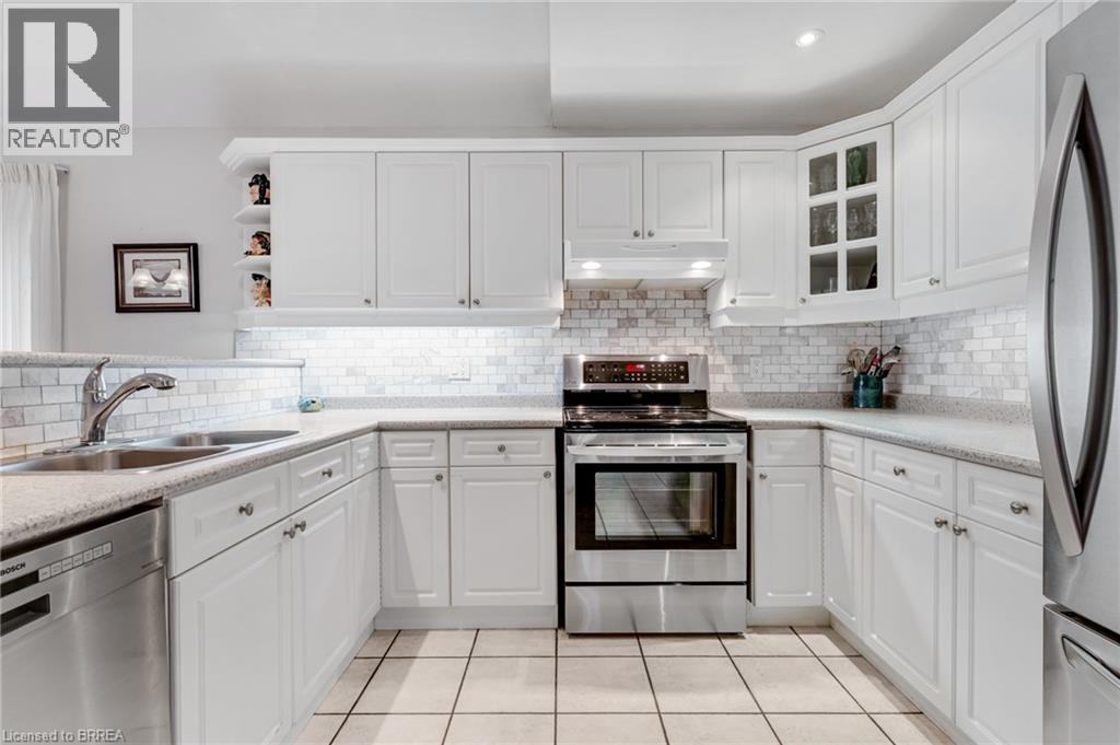 U-shaped kitchen featuring white cabinetry, light-toned countertops, subway tile backsplash, stainless steel appliances, and square floor tiles - 422 Powerline Road Unit# 10, Brantford, ON - Indoor Photo Showing Kitchen With Stainless Steel Kitchen With Double Sink