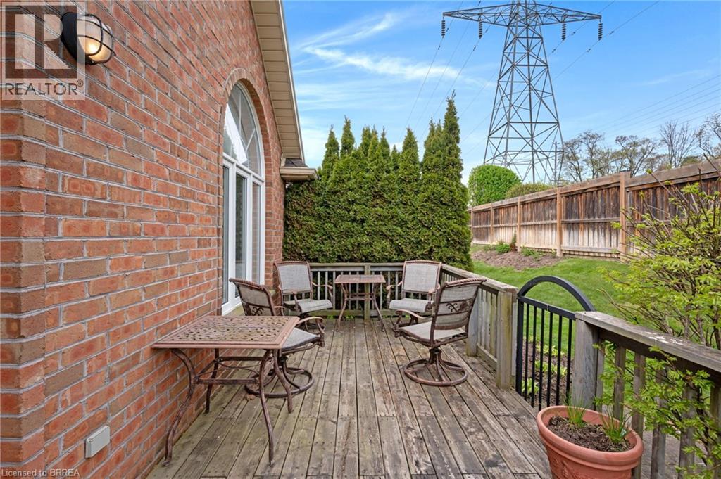 Spacious outdoor wood-finish deck bordered by a wooden privacy fence and mature evergreen trees - 422 Powerline Road Unit# 10, Brantford, ON - Outdoor With Deck Patio Veranda With Exterior