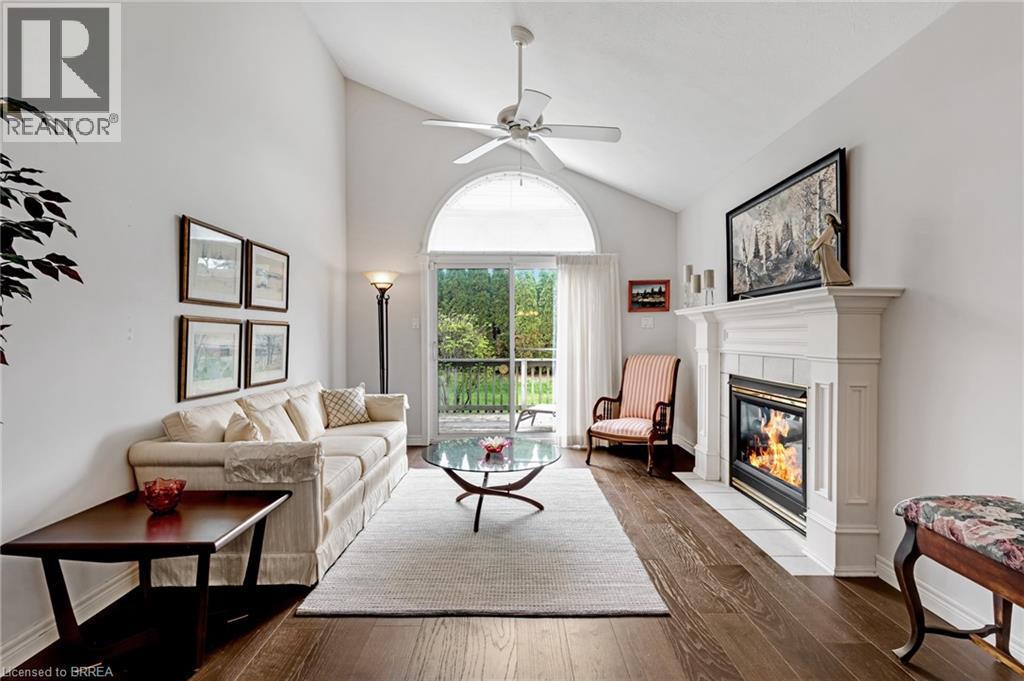 Living area featuring vaulted ceilings, a prominent fireplace with a white mantel, wood-finish flooring, and a large sliding glass door with an arched transom window opening to an outdoor deck - 422 Powerline Road Unit# 10, Brantford, ON - Indoor Photo Showing Living Room With Fireplace