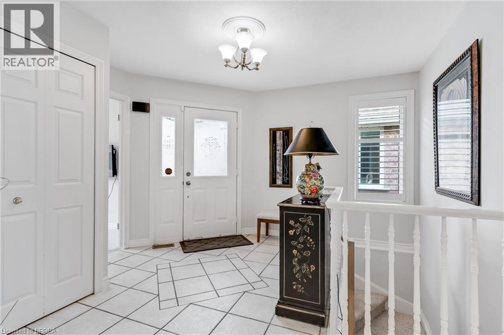 Entryway featuring white square tile flooring with a geometric inlay, a white front door with frosted glass inserts, and an overhead three-light fixture - 422 Powerline Road Unit# 10, Brantford, ON - Indoor Photo Showing Other Room
