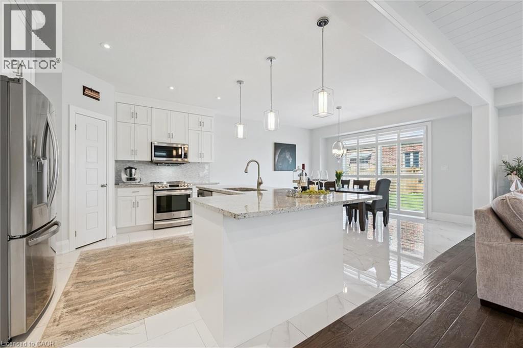 Bright kitchen featuring white cabinetry, stainless steel appliances, a white island with a stone countertop, and pendant lighting - 72 Elmbank Trail, Kitchener, ON - Indoor Photo Showing Kitchen With Upgraded Kitchen
