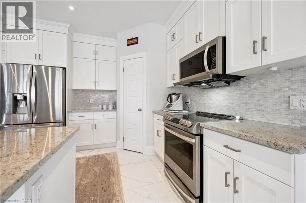White kitchen featuring stainless steel appliances, granite countertops, white shaker cabinetry, and a mosaic tile backsplash - 72 Elmbank Trail, Kitchener, ON - Indoor Photo Showing Kitchen With Upgraded Kitchen
