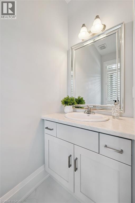 Vanity featuring a white countertop with an undermount sink, white cabinetry with dark hardware, a large framed mirror, and a two-bulb wall sconce - 72 Elmbank Trail, Kitchener, ON - Indoor Photo Showing Bathroom