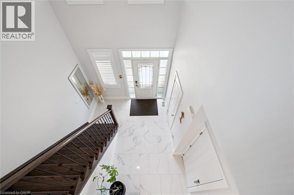 Two-story foyer featuring wood-finish staircase with wrought iron balusters, white marble-look flooring, and a glass-paneled entry door with sidelights - 72 Elmbank Trail, Kitchener, ON - Indoor Photo Showing Other Room