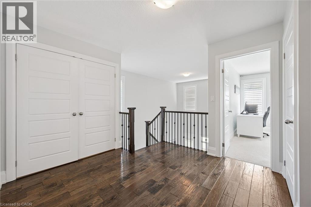 Upper landing featuring wood-finish flooring, white paneled doors, and a staircase with dark wood handrail and black metal balusters - 72 Elmbank Trail, Kitchener, ON - Indoor Photo Showing Other Room