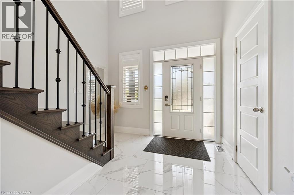 Bright entryway featuring white marble-look tile flooring, a white paneled entry door with frosted sidelights and transom windows, and a dark wood staircase with black iron balusters - 72 Elmbank Trail, Kitchener, ON - Indoor Photo Showing Other Room