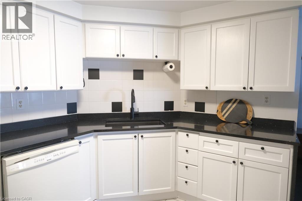 White shaker cabinetry with dark hardware and a black countertop featuring an integrated sink - 175 Hunter Street E Unit# 301, Hamilton, ON - Indoor Photo Showing Kitchen