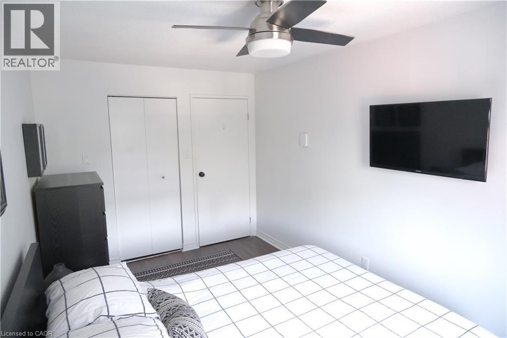 Bright interior space featuring wood-finish flooring, a contemporary ceiling fan, and two white doors - 175 Hunter Street E Unit# 301, Hamilton, ON - Indoor Photo Showing Bedroom