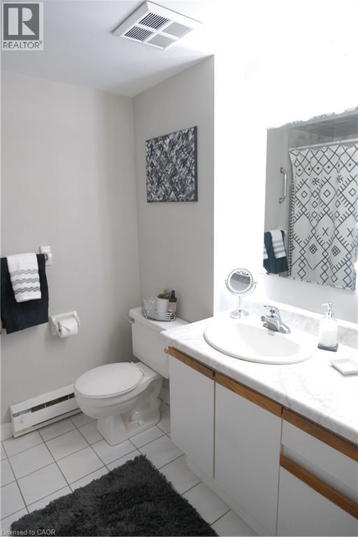 Bathroom featuring white tile flooring, a white toilet, and a vanity with white cabinetry, a light-colored countertop, and an integrated sink - 175 Hunter Street E Unit# 301, Hamilton, ON - Indoor Photo Showing Bathroom