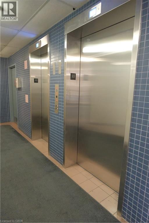 Dual stainless steel elevators set within a hallway featuring blue square tile walls and a grey carpet runner - 175 Hunter Street E Unit# 301, Hamilton, ON - Indoor