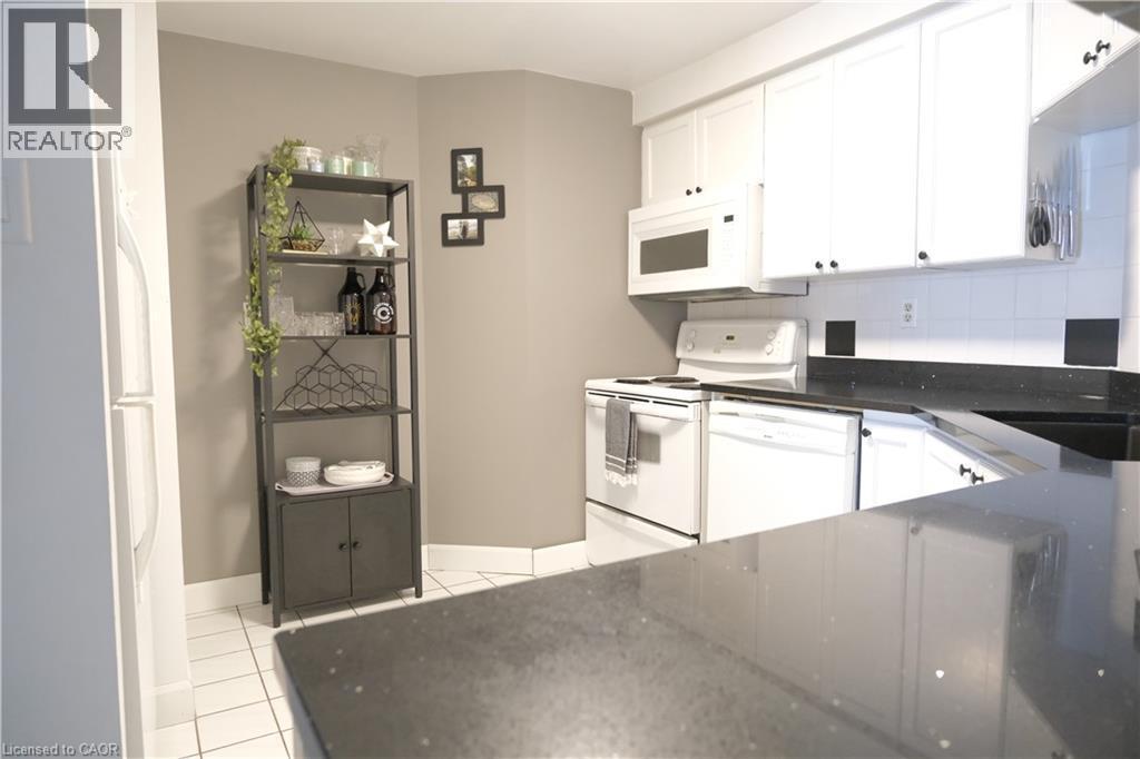 Kitchen featuring white cabinetry, black countertops, white subway tile backsplash, and white appliances including a range, microwave, and dishwasher - 175 Hunter Street E Unit# 301, Hamilton, ON - Indoor Photo Showing Kitchen