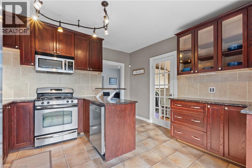 Kitchen featuring wood cabinetry, stainless steel appliances, dark countertops, beige tile backsplash, and light-toned tile flooring - 204 Beach Boulevard, Hamilton, ON - Indoor Photo Showing Kitchen