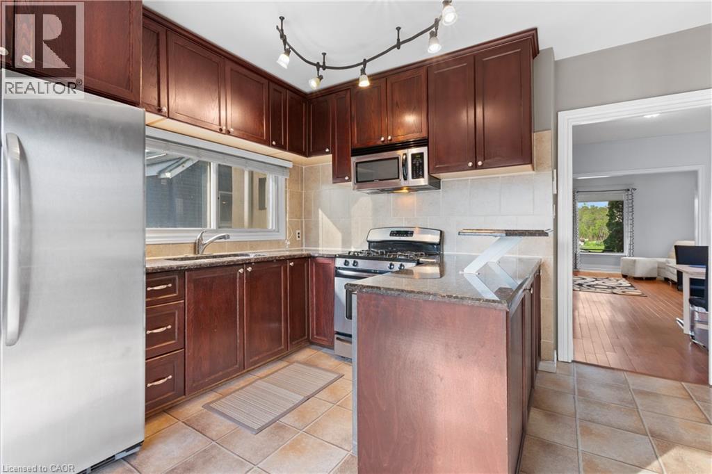 Kitchen featuring dark wood-finish cabinetry, stainless steel appliances, a gas range, a track lighting fixture, and a peninsula with a stone countertop - 204 Beach Boulevard, Hamilton, ON - Indoor Photo Showing Kitchen