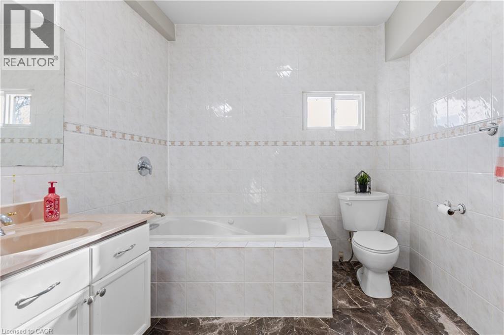 Bathroom featuring a built-in tub, white tiled walls with a decorative border, and a vanity with a light-colored countertop - 204 Beach Boulevard, Hamilton, ON - Indoor Photo Showing Bathroom