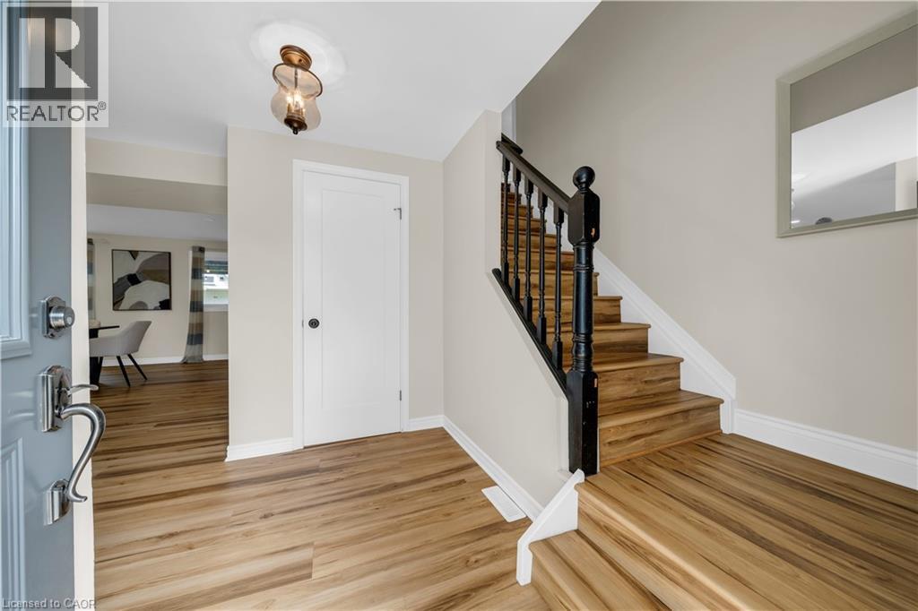 Entryway featuring wood-finish flooring, a staircase with dark wood newel posts and spindles, a ceiling-mounted light fixture, and a white interior door with dark hardware - 26 Peachtree Crescent, Cambridge, ON - Indoor Photo Showing Other Room
