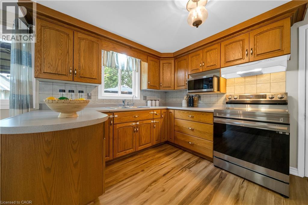 Kitchen featuring wood cabinetry, light-toned countertops, tile backsplash, stainless steel range, and wood-finish flooring - 26 Peachtree Crescent, Cambridge, ON - Indoor Photo Showing Kitchen