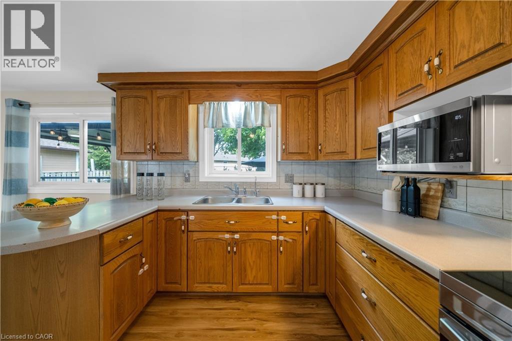 Kitchen featuring wood cabinetry, a double basin sink, light-toned countertops, tile backsplash, and wood-finish flooring - 26 Peachtree Crescent, Cambridge, ON - Indoor Photo Showing Kitchen With Double Sink