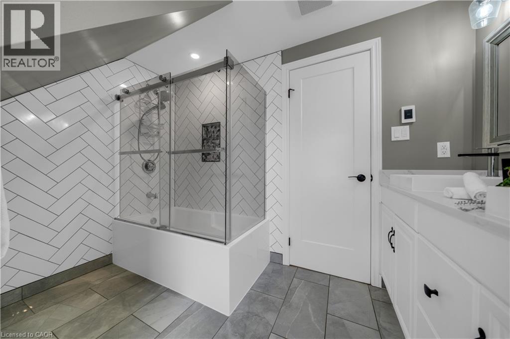 Contemporary bathroom featuring a bathtub with a sliding glass enclosure, herringbone pattern wall tile, and recessed lighting - 26 Peachtree Crescent, Cambridge, ON - Indoor Photo Showing Bathroom