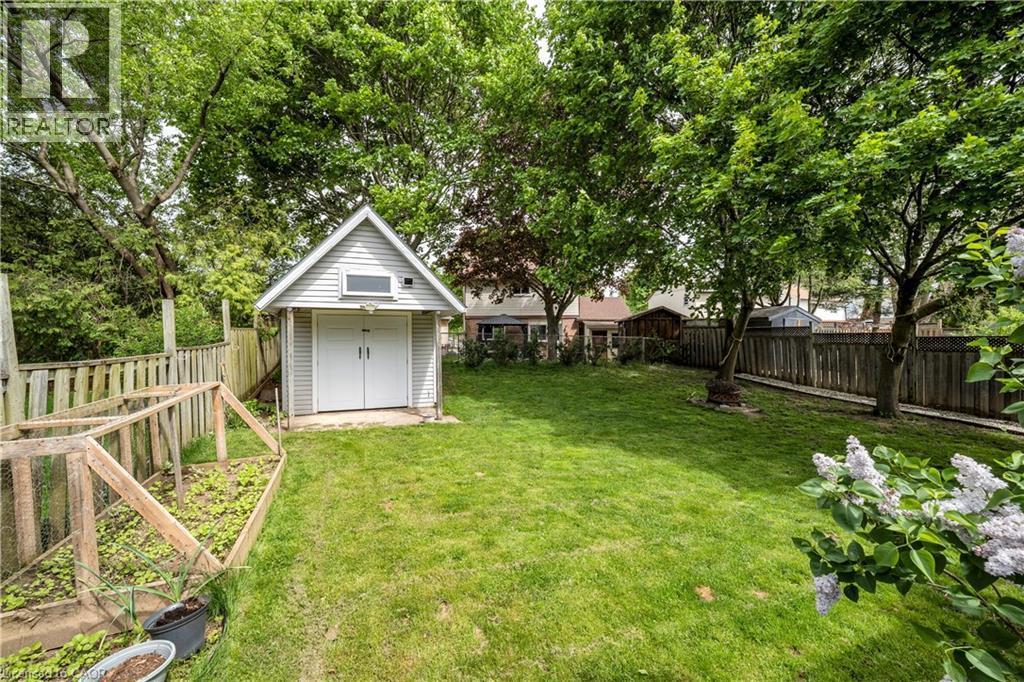 Expansive backyard featuring a gabled storage shed with double white doors, an enclosed garden bed, mature trees, and privacy fencing - 26 Peachtree Crescent, Cambridge, ON - Outdoor With Backyard