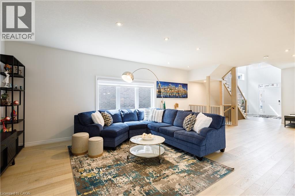 Open-concept living area featuring light wood-finish flooring, a wall of windows, recessed lighting, and a prominent staircase with light wood banisters - 581 Doonwoods Crescent, Kitchener, ON - Indoor Photo Showing Living Room