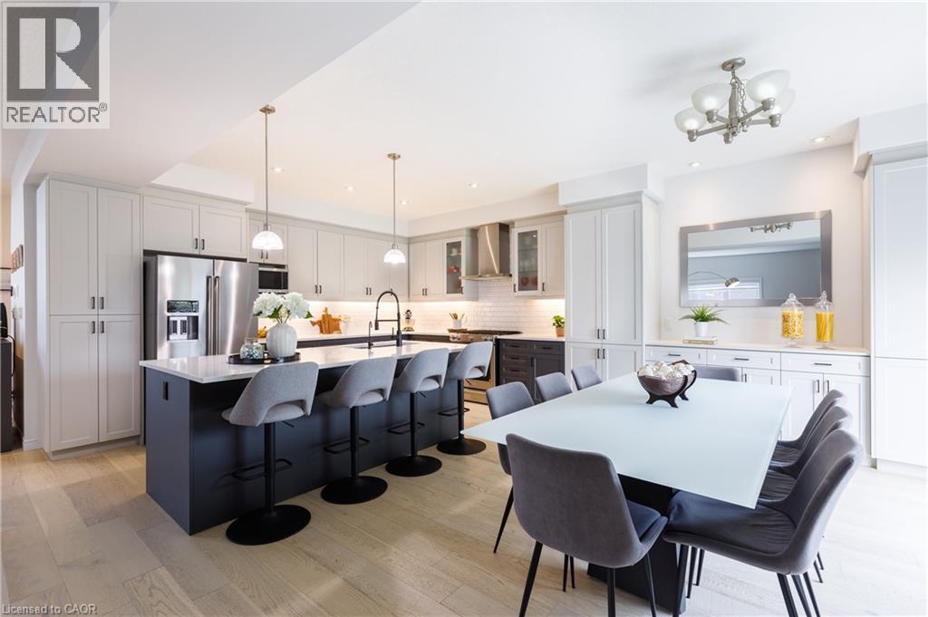 Open-concept kitchen featuring an oversized island with seating, pendant lighting, stainless steel appliances, and light wood-finish flooring - 581 Doonwoods Crescent, Kitchener, ON - Indoor